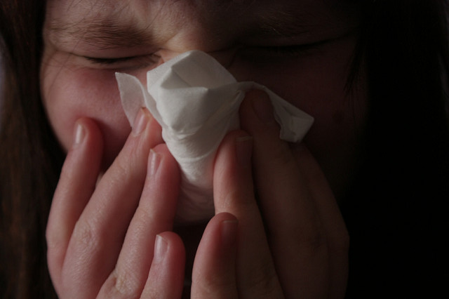 young girl blowing nose into tissue