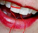 floss wrapped around young woman's tooth, red lipstick